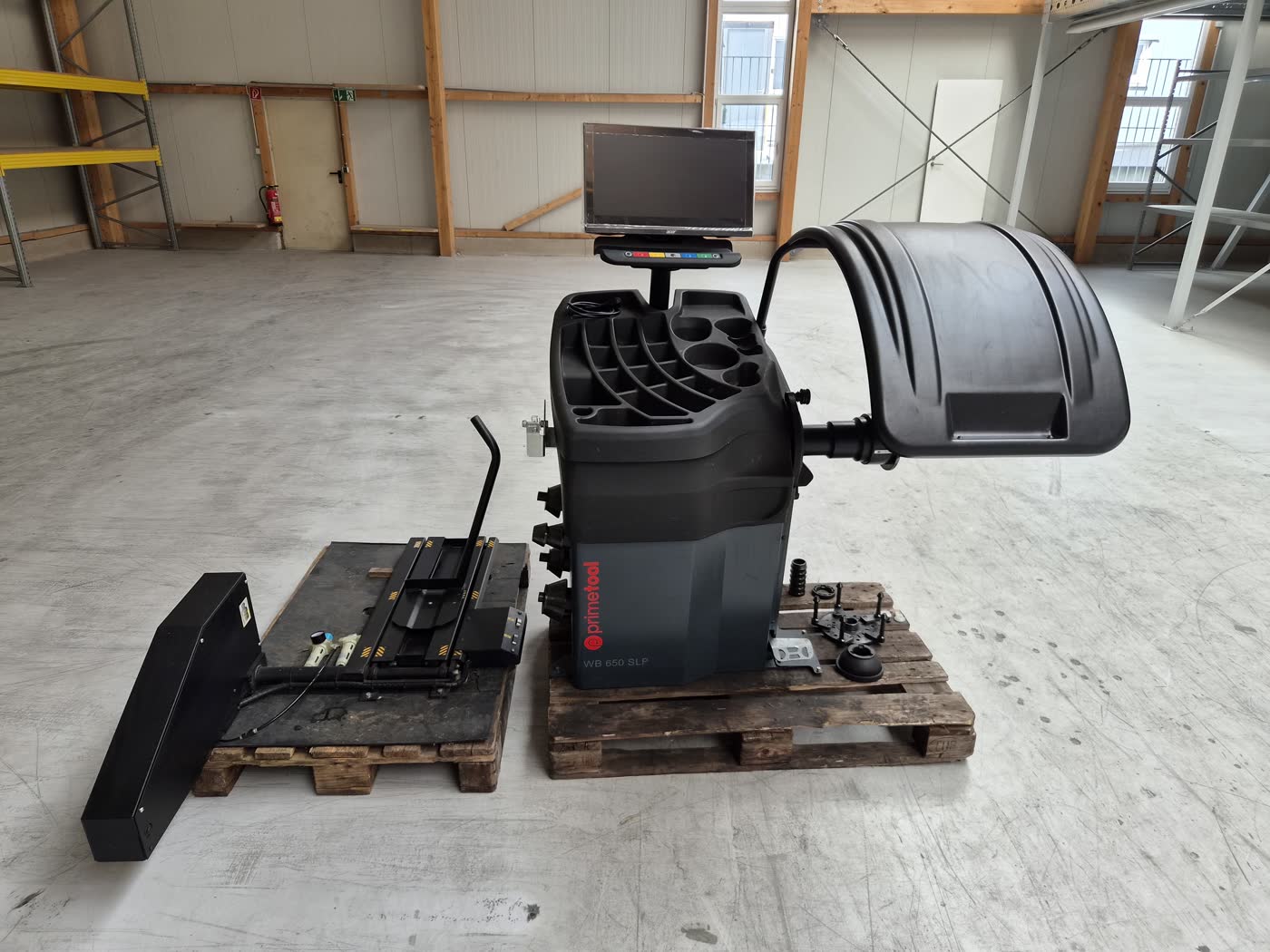 Wuchtmaschine WB 650 SLP und Radlift auf zwei Holzpaletten in einer Lagerhalle